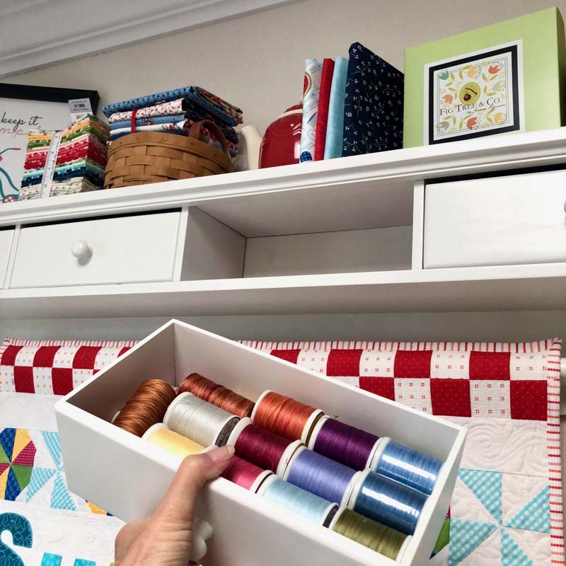 Thread storage tucked inside drawers of a shelf unit.