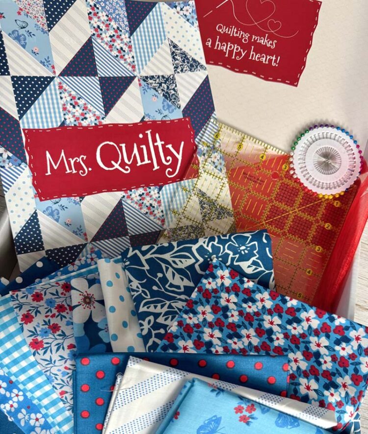 Contents of Mrs. Quilty subscription box month 1 include 12 fat quarters in blues with a pop of red, magazine, 6.5" square ruler and straight pins.