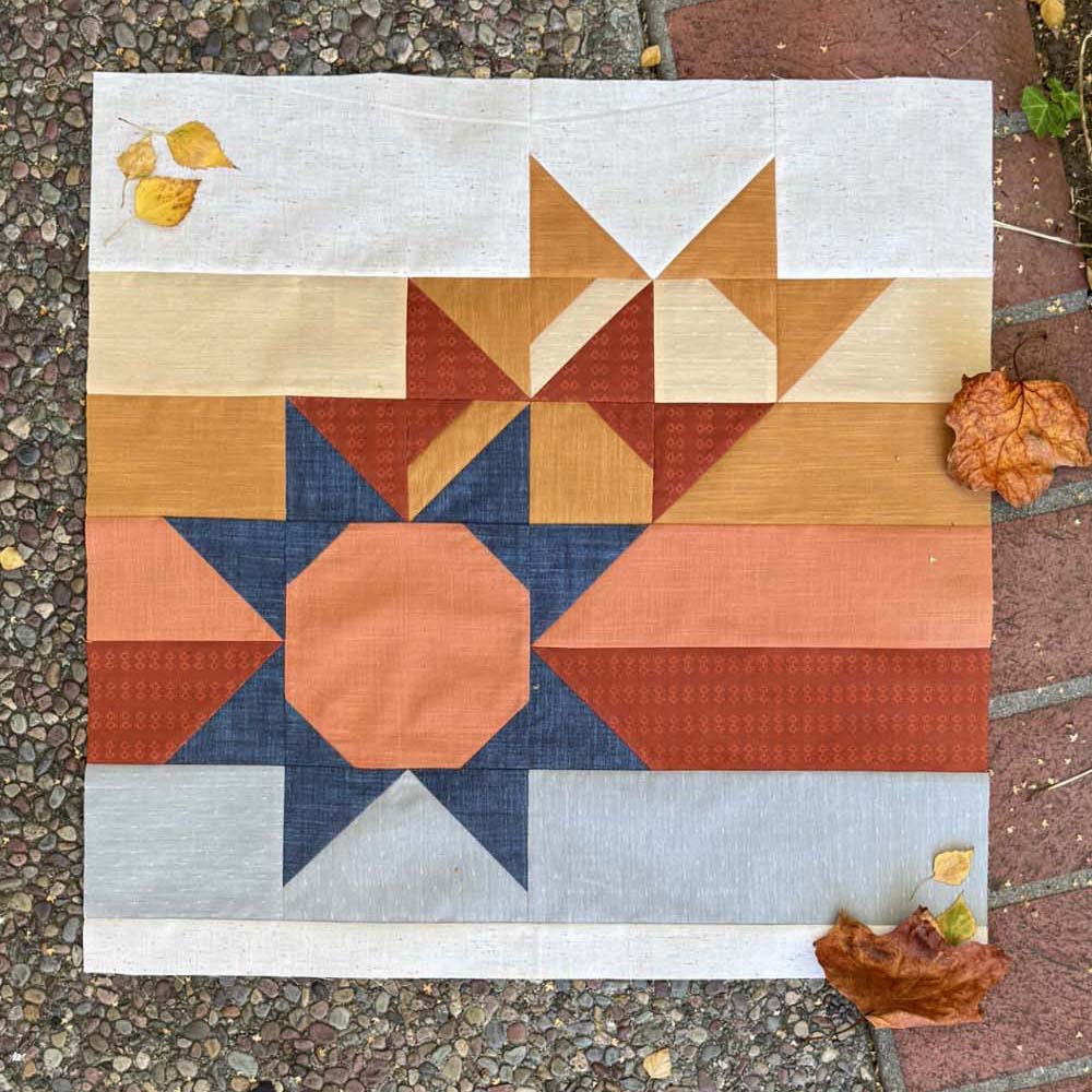 Sun Still quilt block on the ground with a few fall leaves.