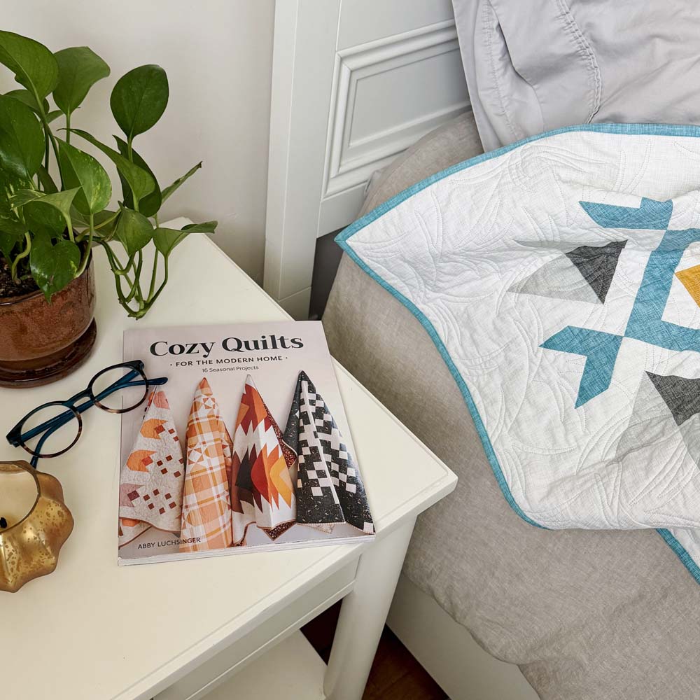 Cozy Quilts book on a nightstand with reading glasses