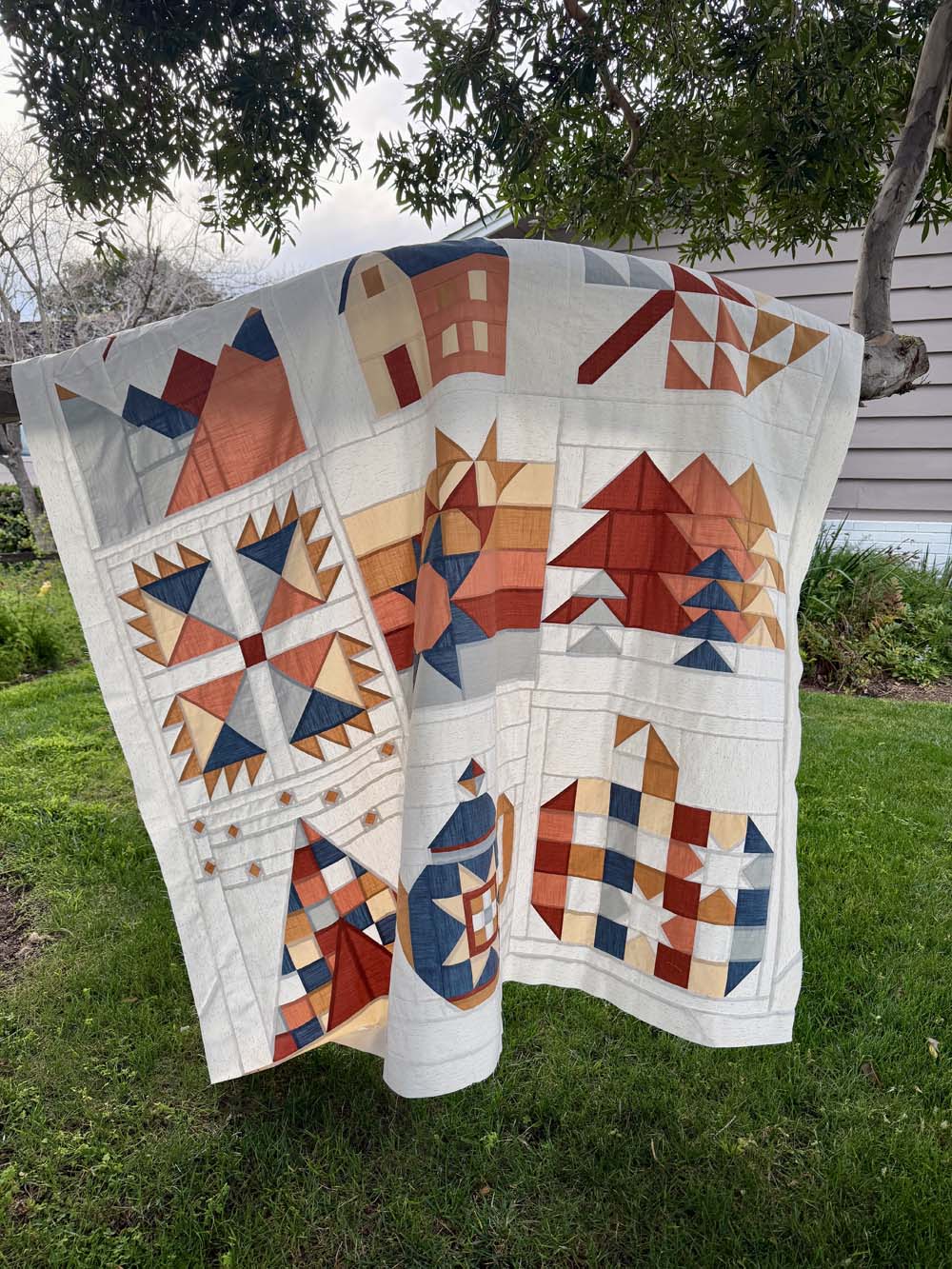 My finished Sweater Weather Quilt Top hanging from a tree branch outside.